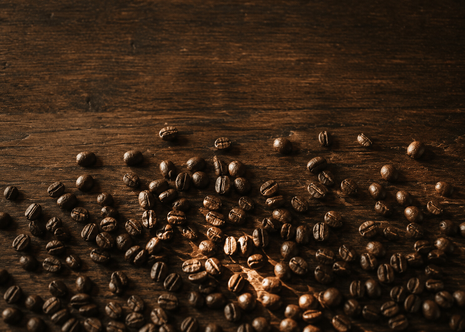 Whole coffee beans scattered across a dark wooden surface in warm light.