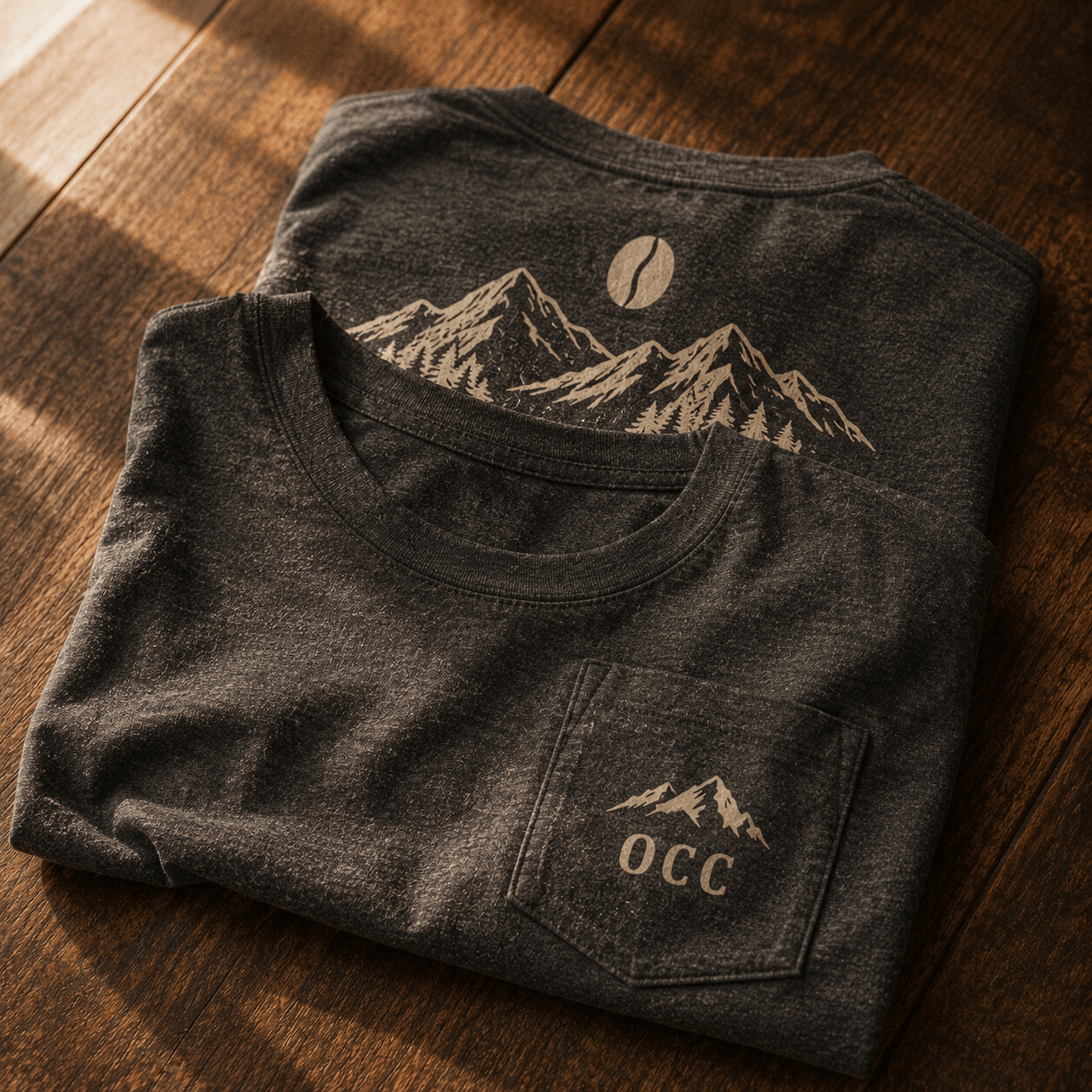 A heather-charcoal t-shirt with a chest-pocket logo and a larger mountain-and-coffee-bean graphic on the back.
